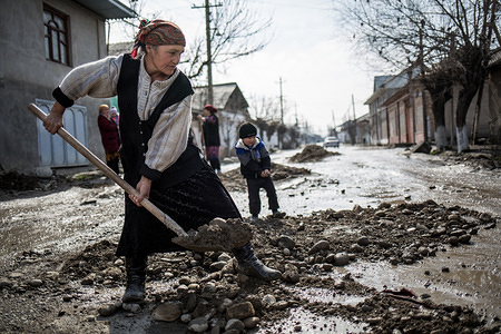 An elderly woman shovels mud from a destroyed road near her house. 

Families left behind is a reality in Central Asia, a region that has more than 10 million migrants on the move looking for better employment and living opportunities beyond the borders of their countries. As migration of both men and women, from Tajikistan, Kyrgyzstan and Uzbekistan, will continue to increase, the number of dependents left behind (children, wives, elderly parents etc.) will rise as well. Migrant workers’ families are waiting and barely surviving while their loved ones are trying to make ends meet in Russia and/or Kazakhstan. Many Central Asian children are growing up without seeing their fathers or mothers, or being left behind when both parents are taking the migration route. Currently more and more women are becoming breadwinners as well, changing the sociocultural norms in Central Asia where men were leading the migration numbers. There are also a lot of women, abandoned or divorced, with the task of raising the children on their own and assume the care of elderly parents. “Your father/mother comes tomorrow” is a common phrase that millions of children in Central Asia hear when they ask the questions “Where is my father? or Where is my mother? When will he/she come back home”? 
However, no one knows when the “tomorrow” will actually arrive. These children who will grow up without regular contact with their parents will soon be the next generation of adults in the region, making up a significant part of its population.